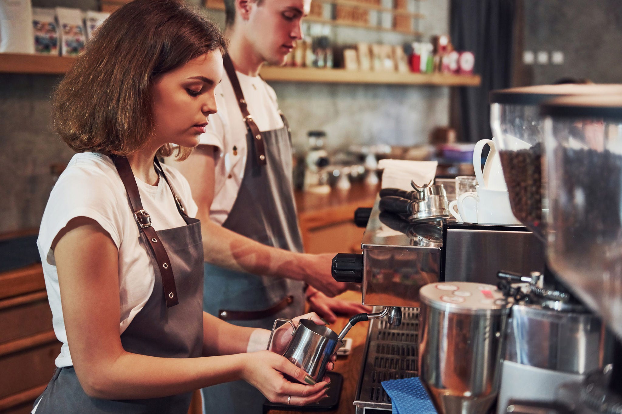 young woman and young man working as baristas in a coffee shop making coffee