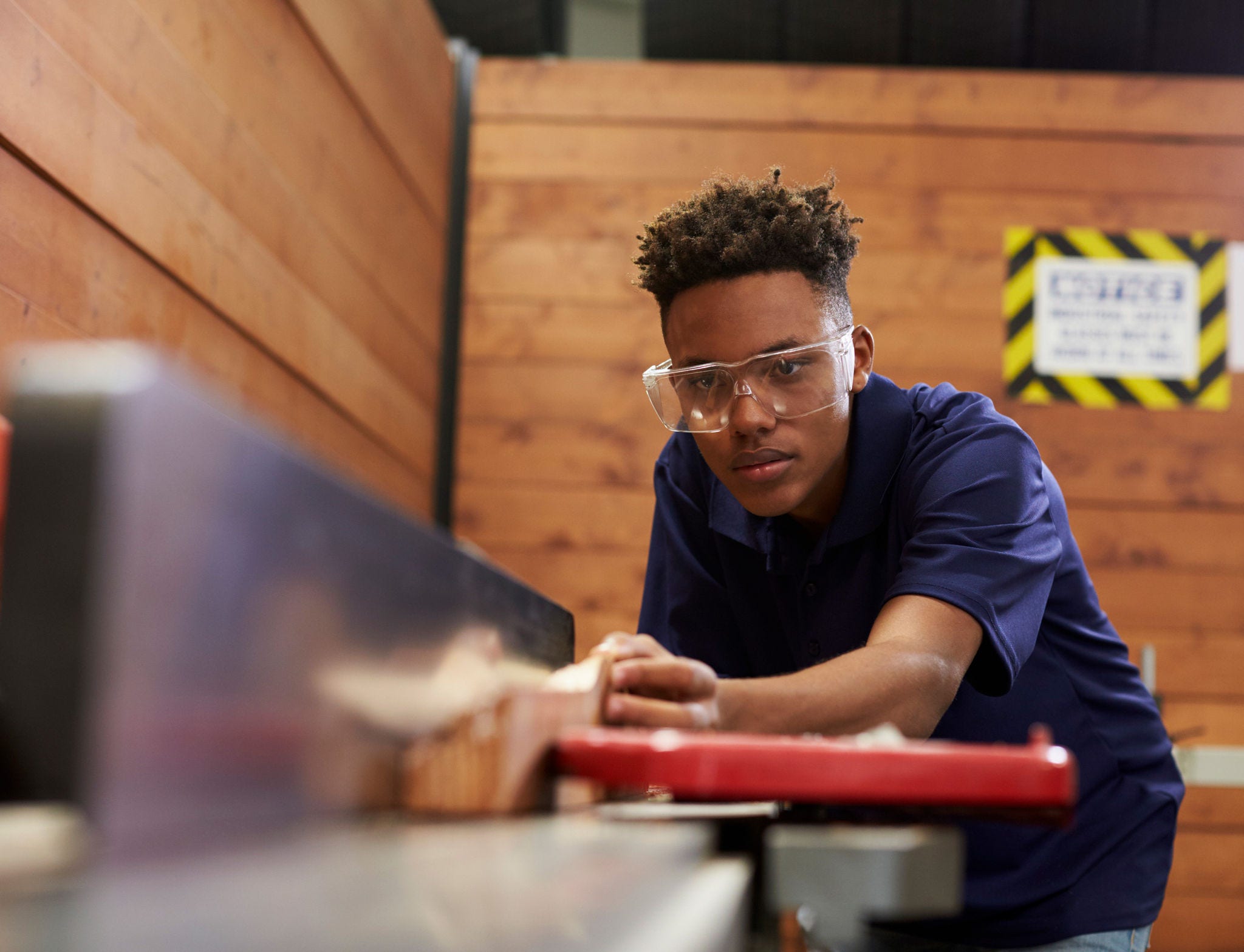 young man wearing safety glasses while cutting wood with a table saw