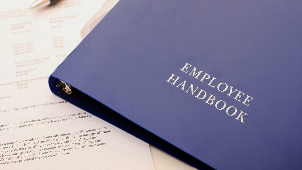 An employee handbook is sitting on top of a blue binder.