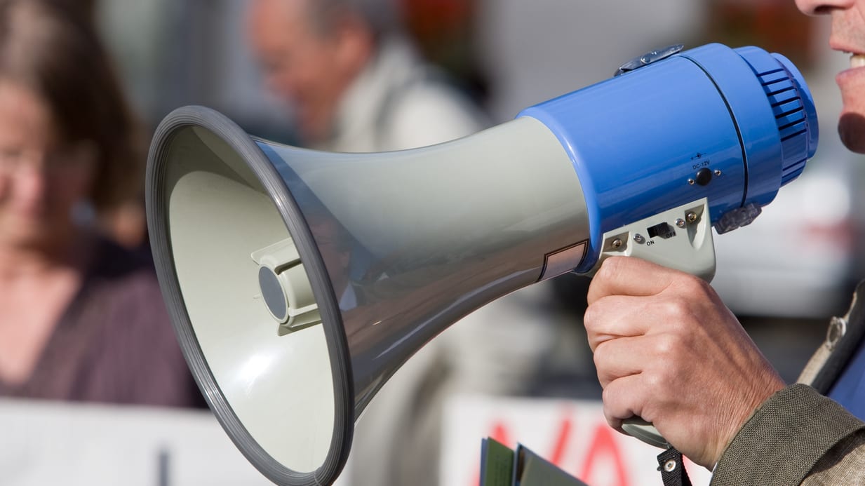 A man holding a megaphone in front of a crowd.