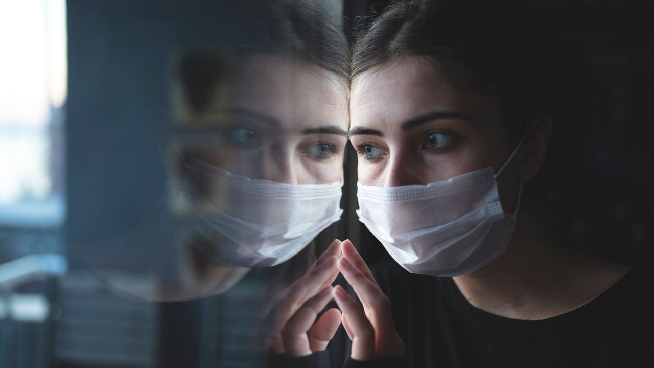A woman wearing a surgical mask in front of a mirror.