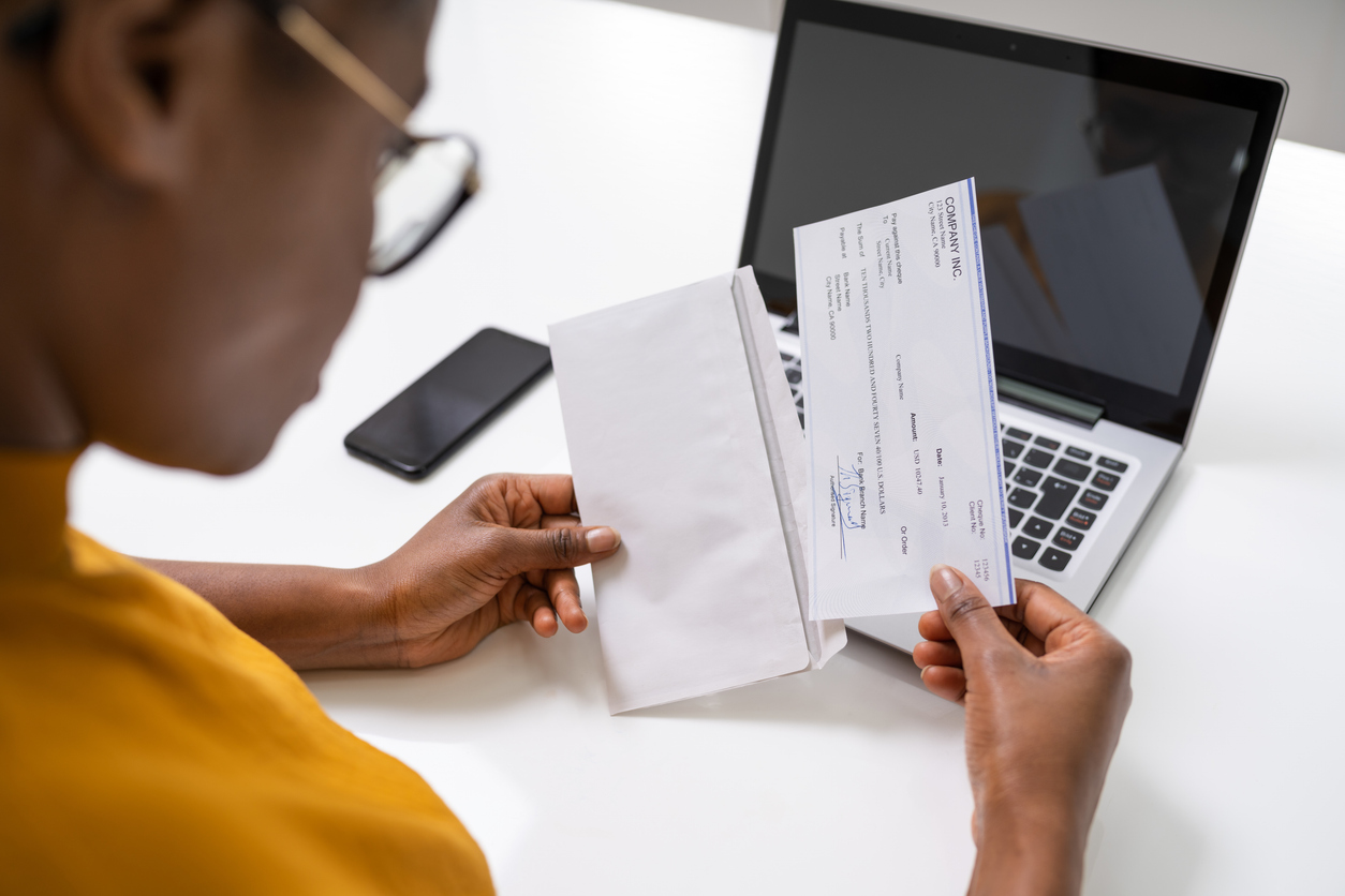 woman looking at a paycheck by a laptop