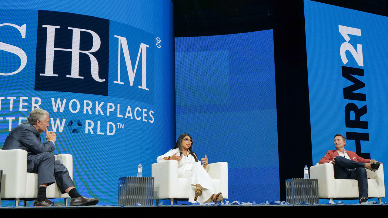 Three people sitting on chairs on stage at the shrm conference.