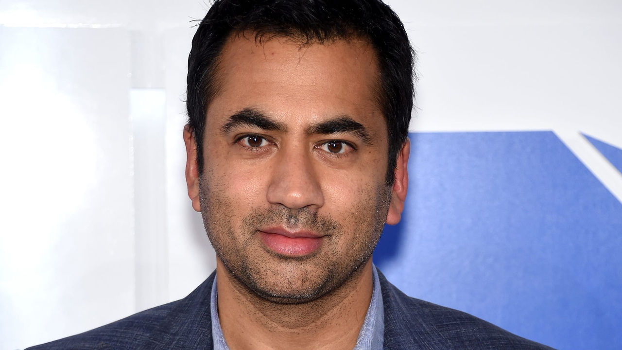 A man in a blue suit standing in front of a blue wall.