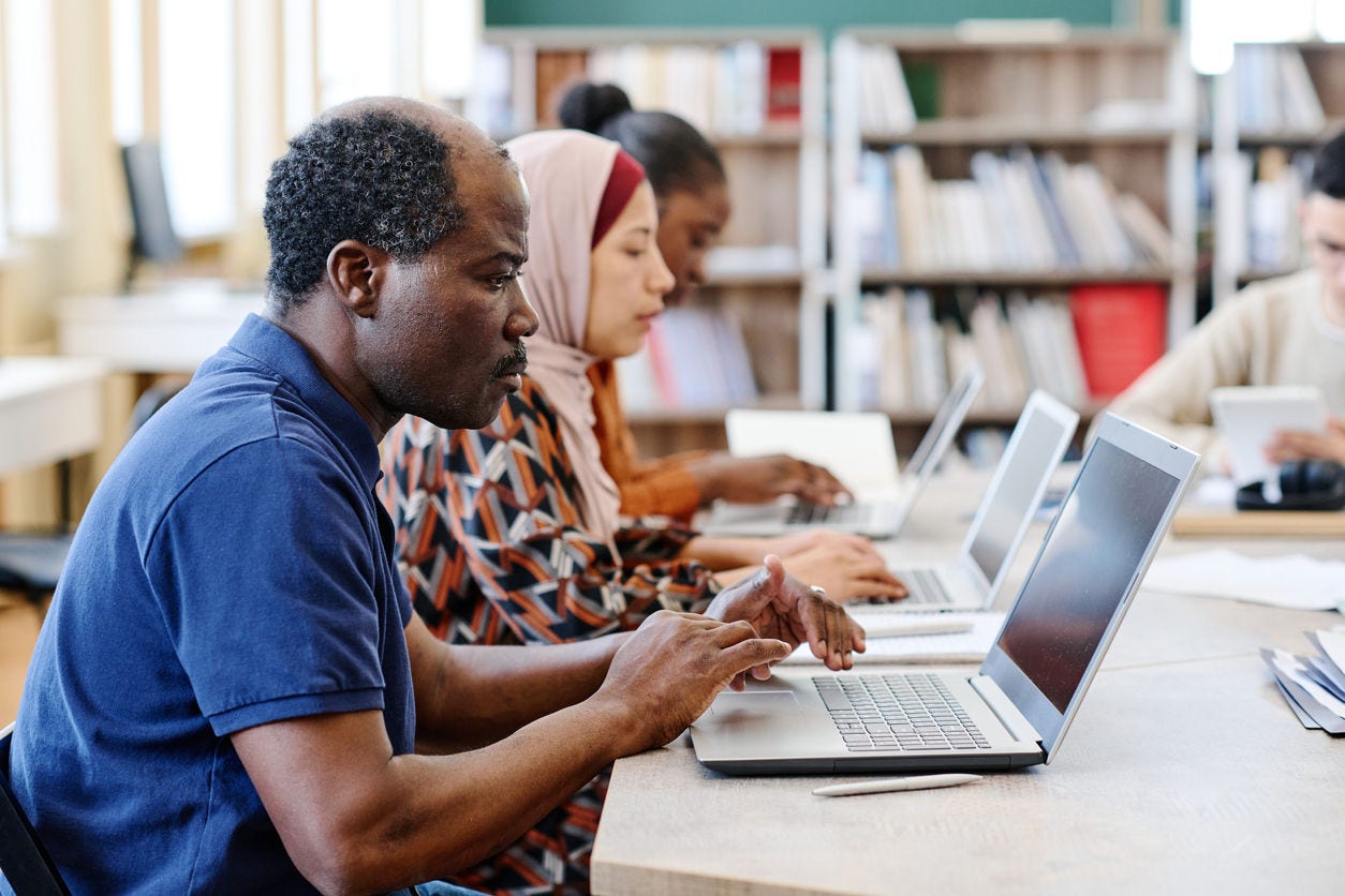 Group of ethnically diverse immigrant students wokring on laptops during lesson searching for information in Internet