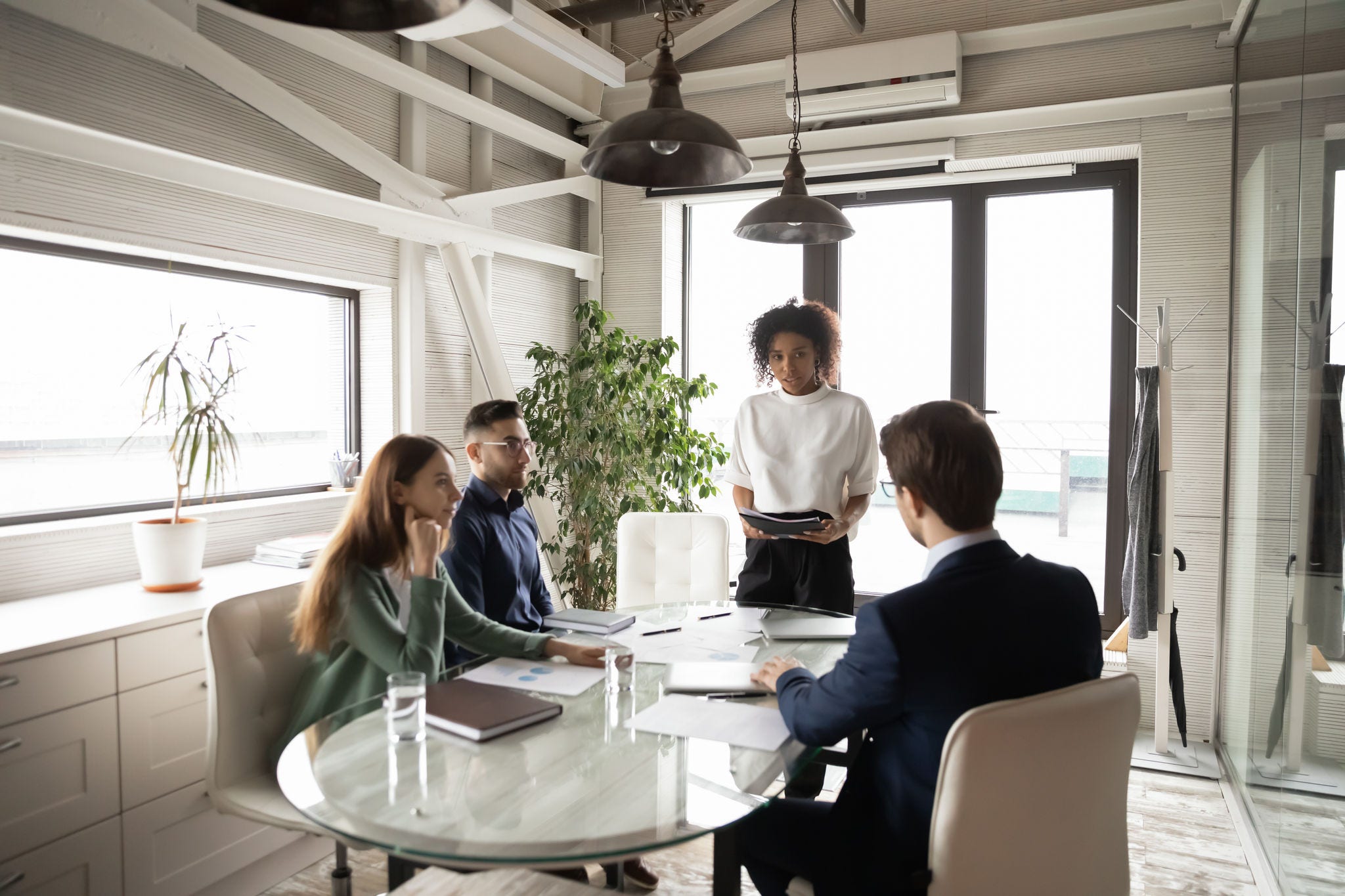 1903208815 Confident African American businesswoman leading briefing, explaining strategy, training diverse staff sitting at table in boardroom, group negotiations, business partners sharing startup ideas