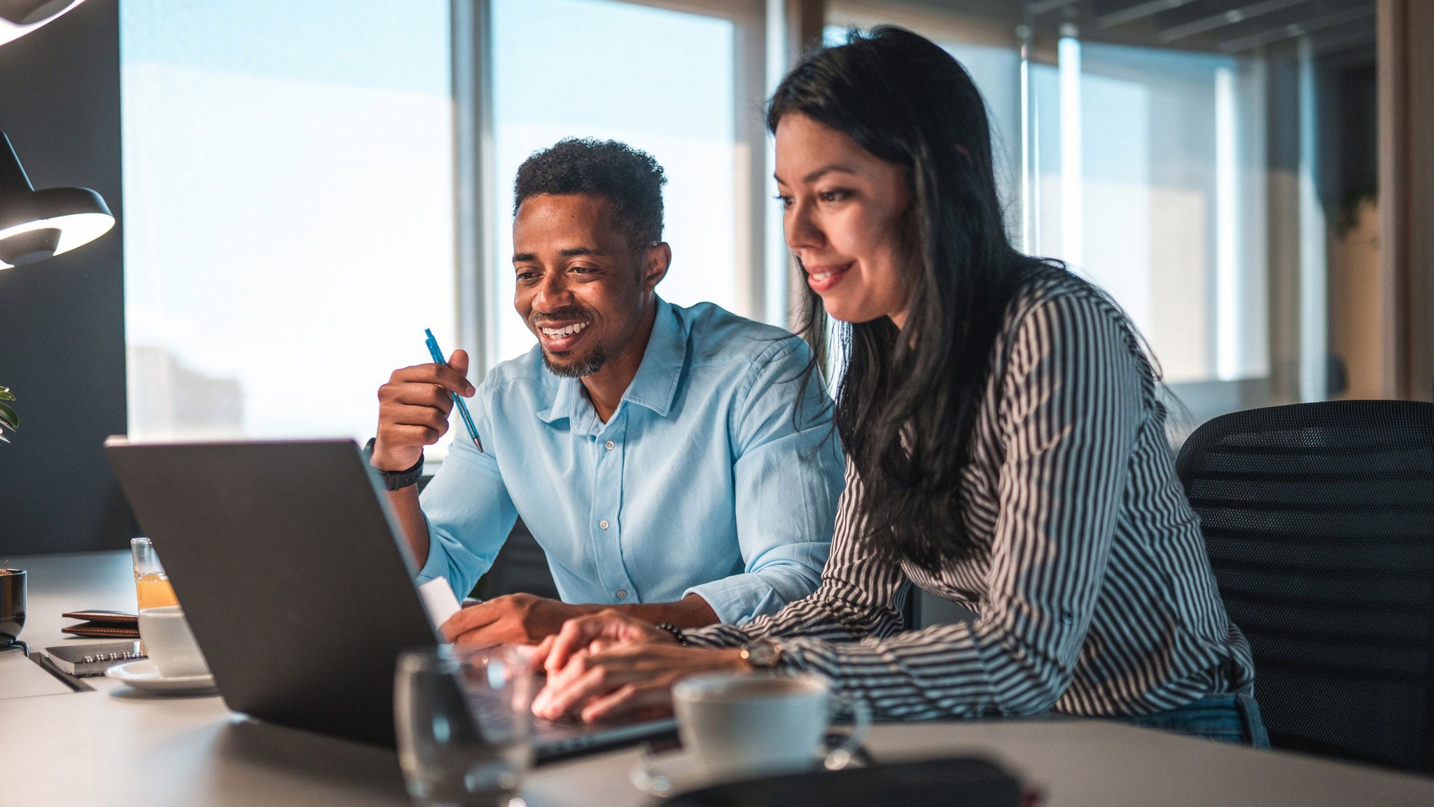 a man and woman work together on a laptop in a conference room in front of a window