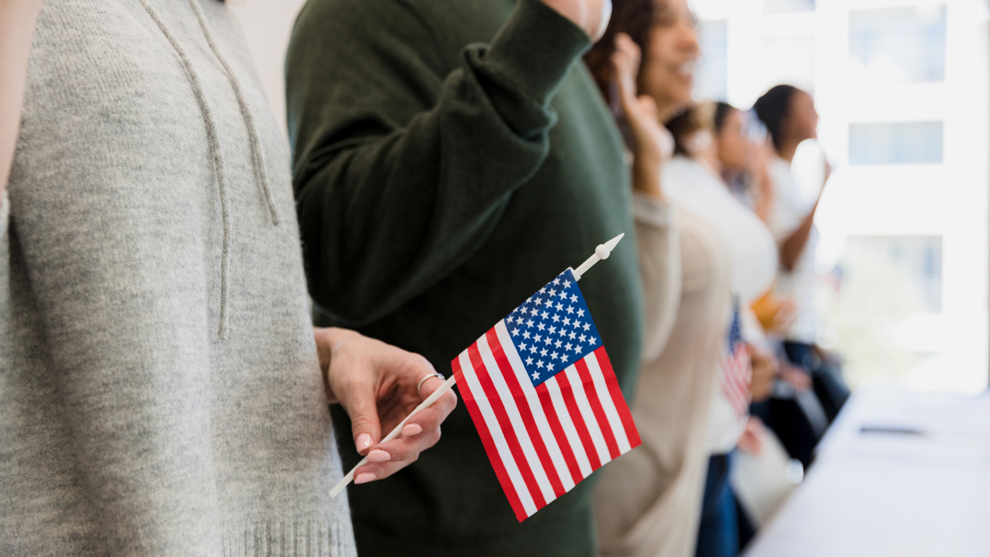a person holds a small american flag while standing in a line with people pledging