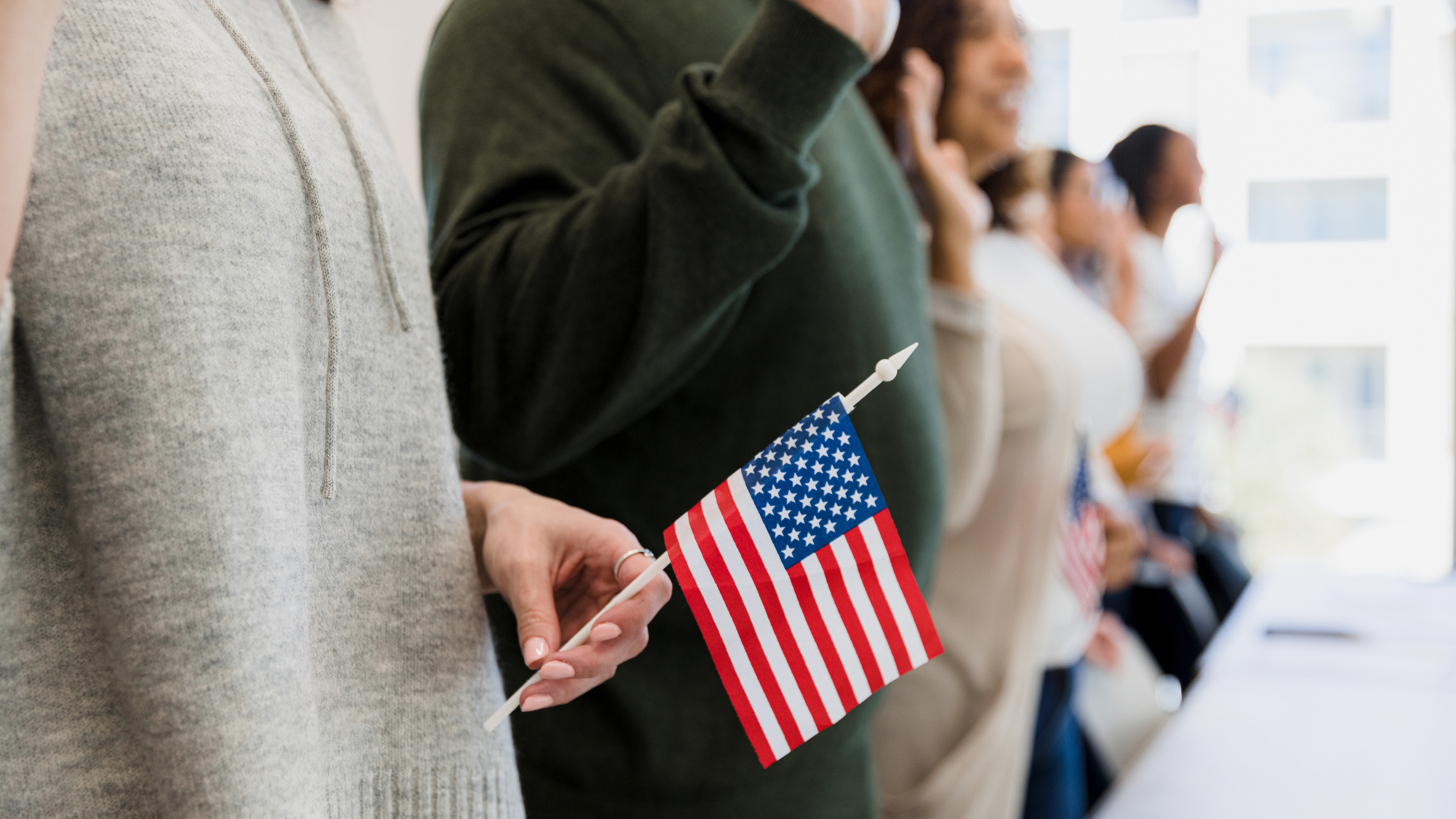 row of people raising their hands pledging while one person holds an american flag