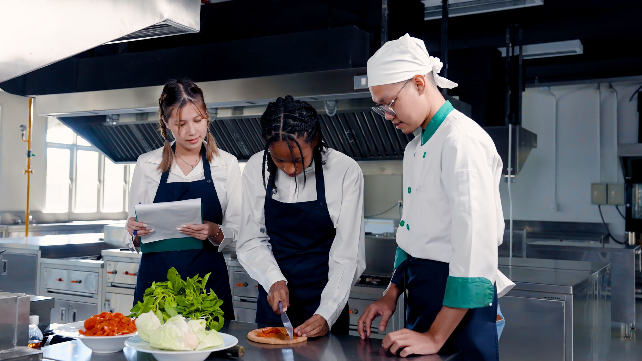 Two young chefs receiving training from other chef in a commercial kitchen