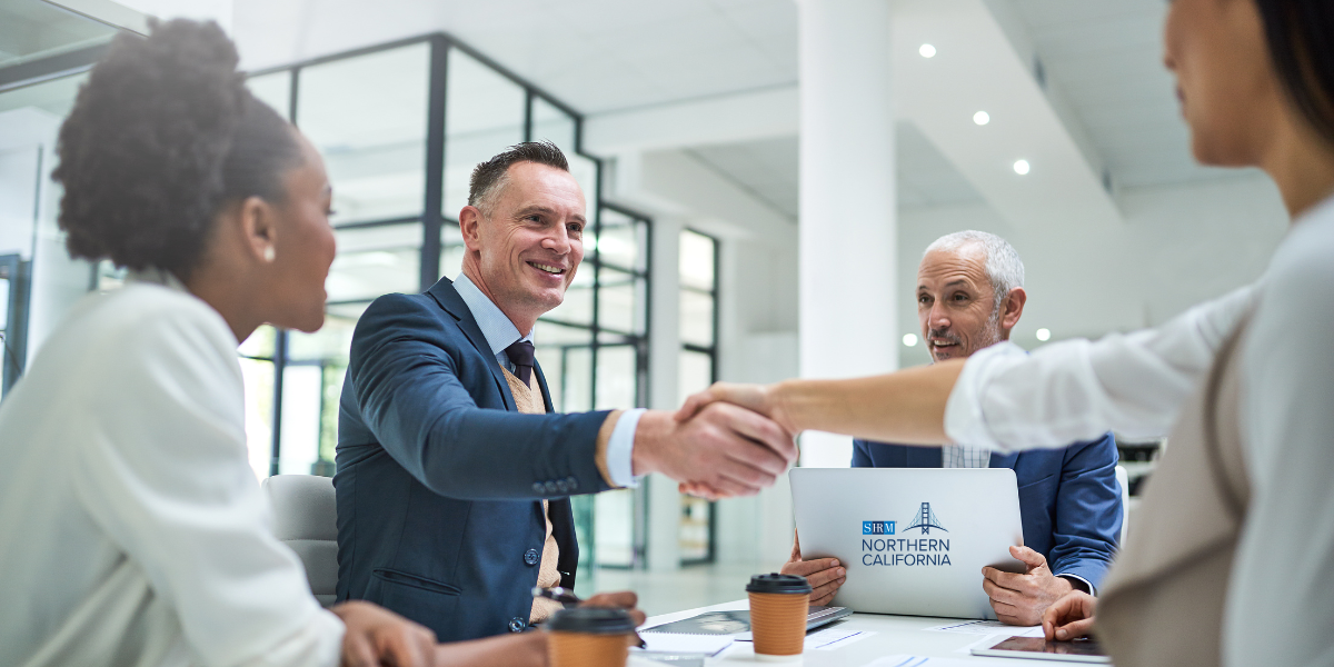 4 people sitting at a table and two are shaking hands