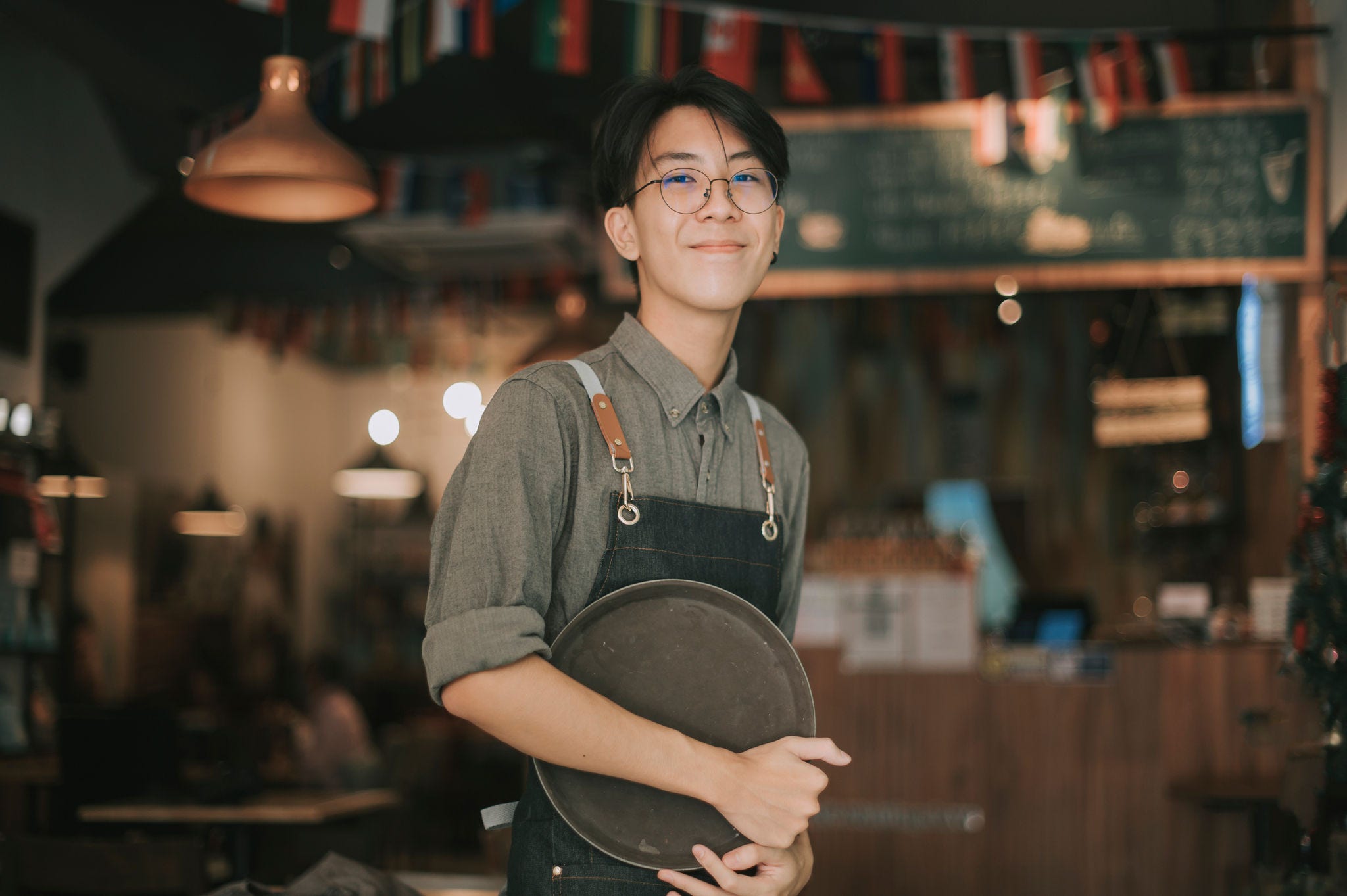 young man working as a barista in a coffee shop holding a serving tray