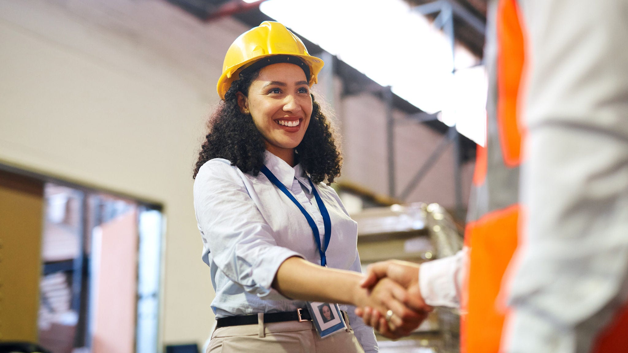 businesswoman wearing a hard hat shakes hands with a construction worker