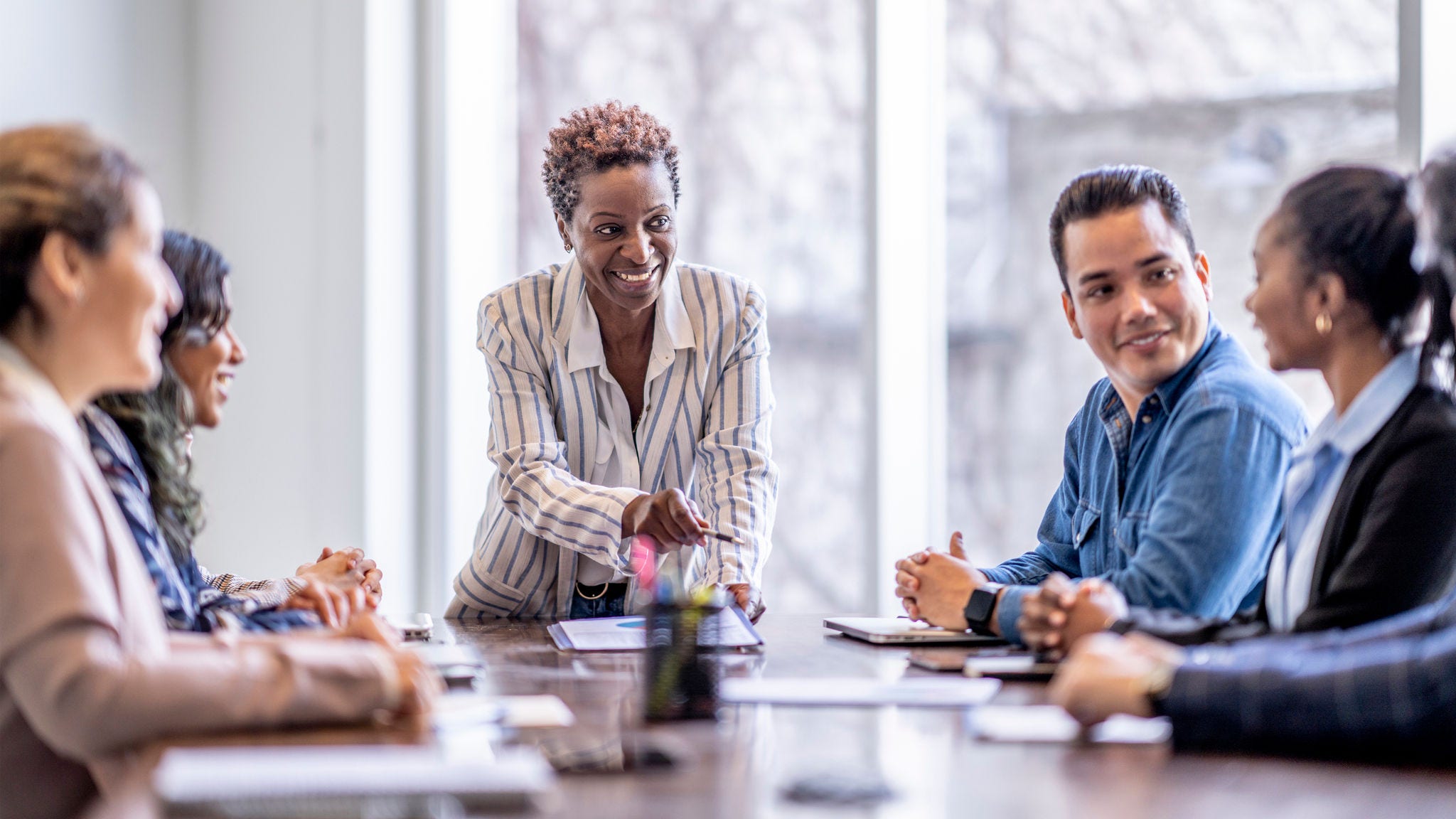 A small group of business professionals sit around a table as they meet to brainstorm some ideas for the future of the company. They are each dressed professionally and have papers scattered out in front of them as they work together. 