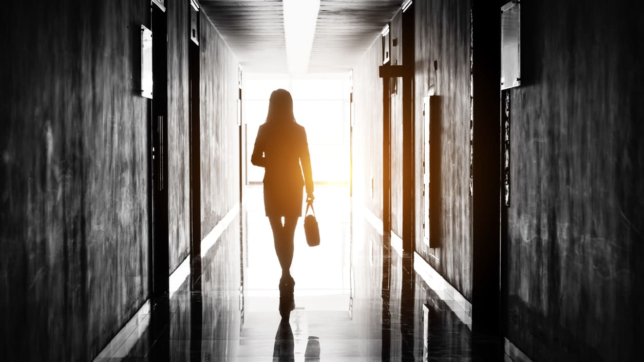 A woman is walking down a hallway with a briefcase.