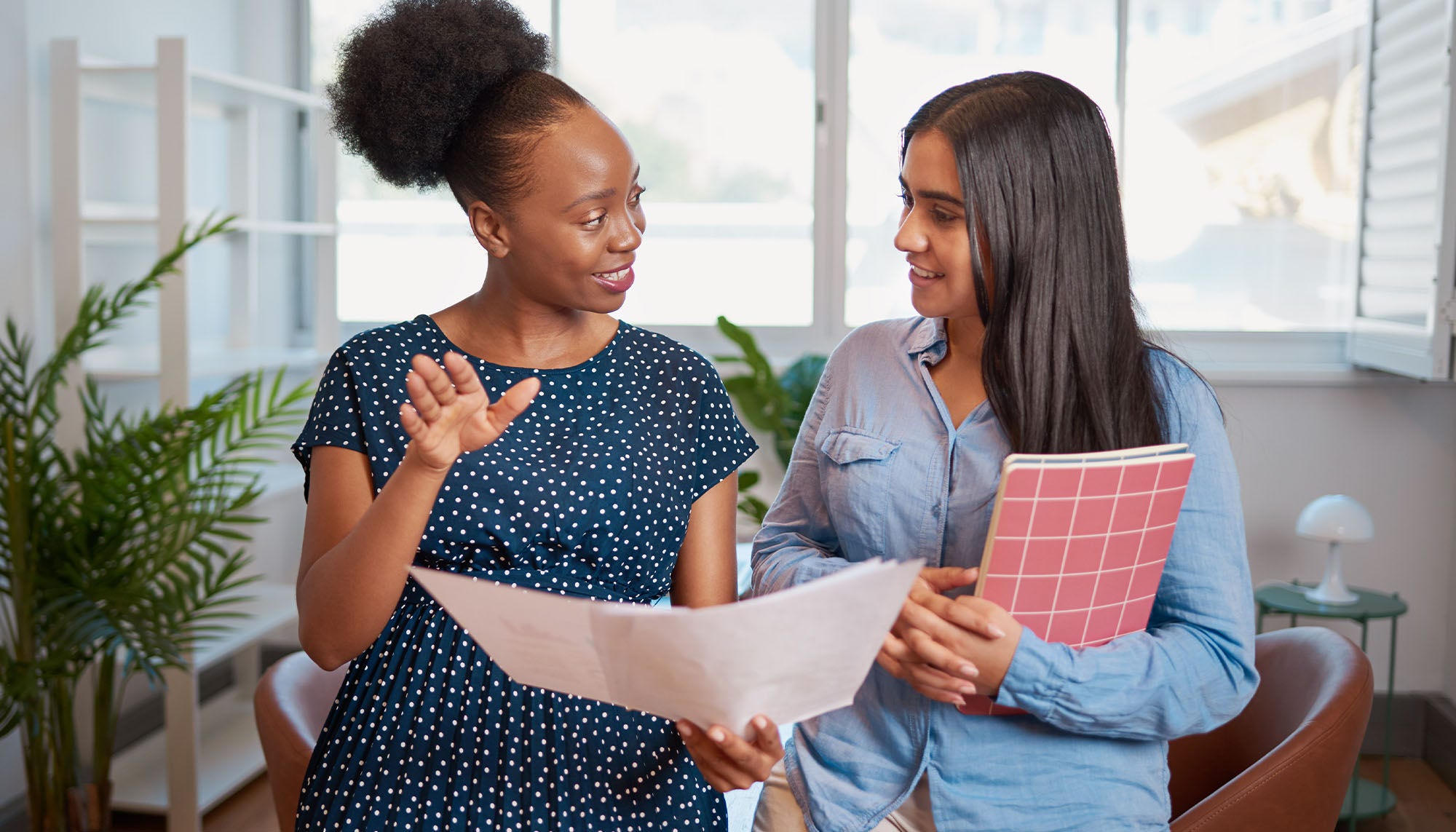 two women collaborating in an office holding papers