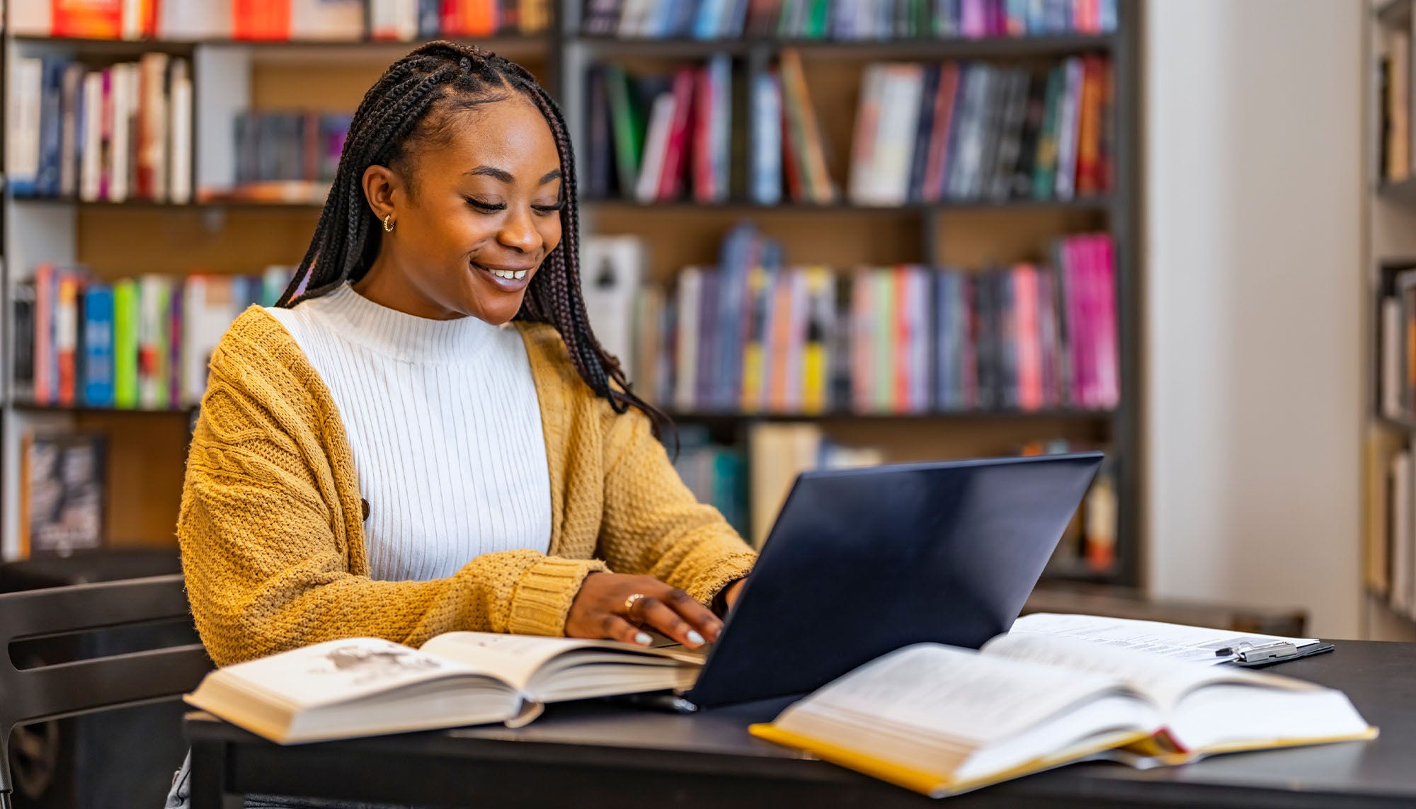 woman works on a laptop in a library surrounded by books