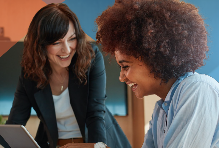 two businesswomen laughing while collaborating in front of a computer