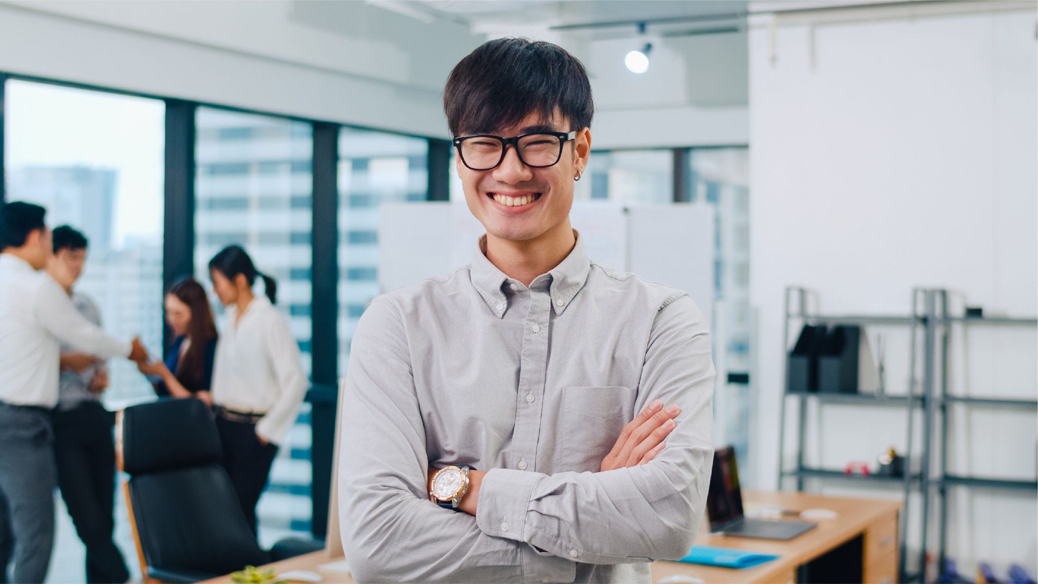 Employee smiles at the camera, while colleagues gather in the background.