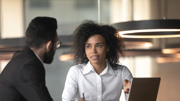 businesswoman speaking to man in modern office in front of laptop