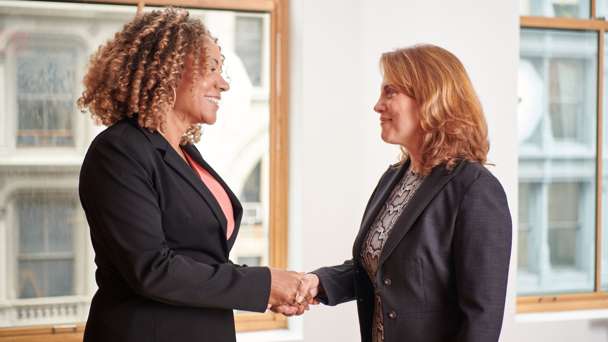 two professional women shaking hands in front of a window