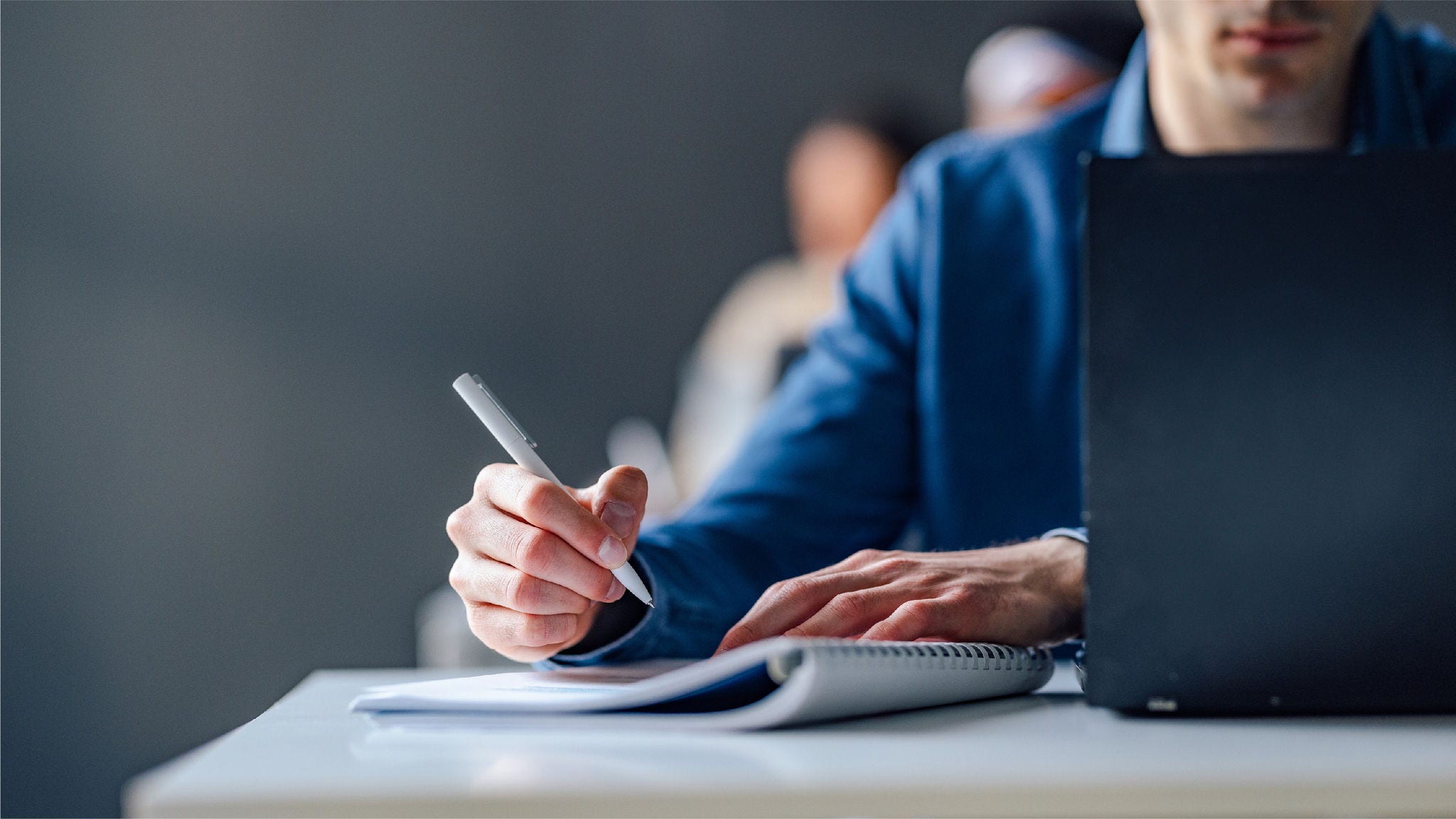 man writing on a notepad next to a laptop