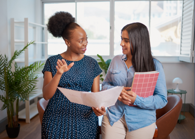 Two women talking in an office environment review paperwork