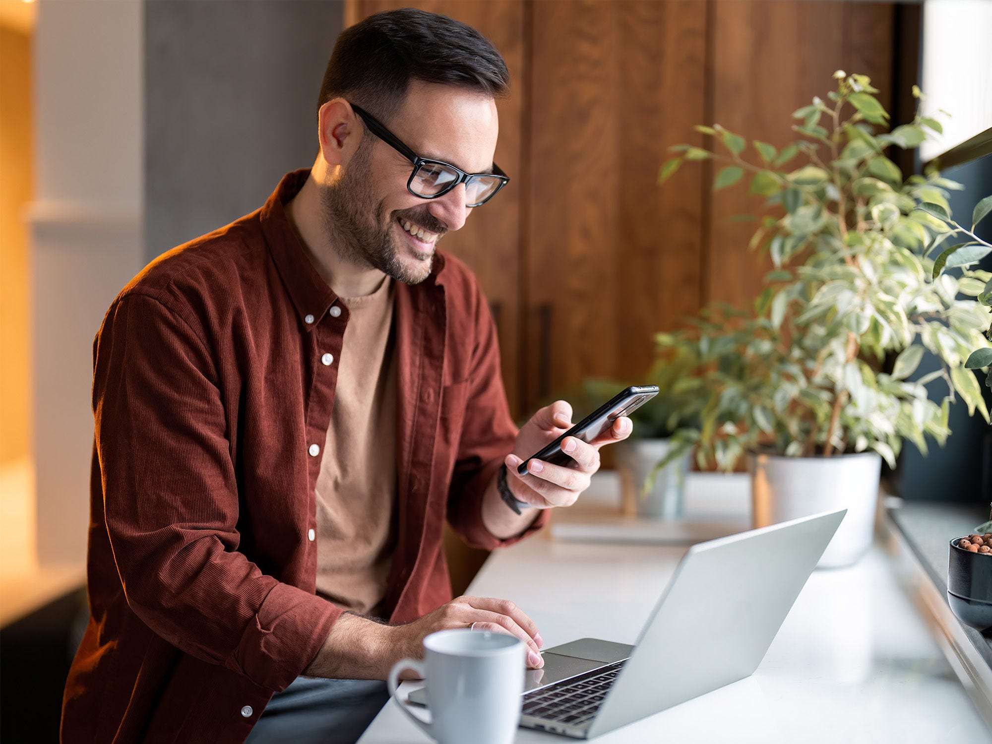 Man smiling at phone working on computer