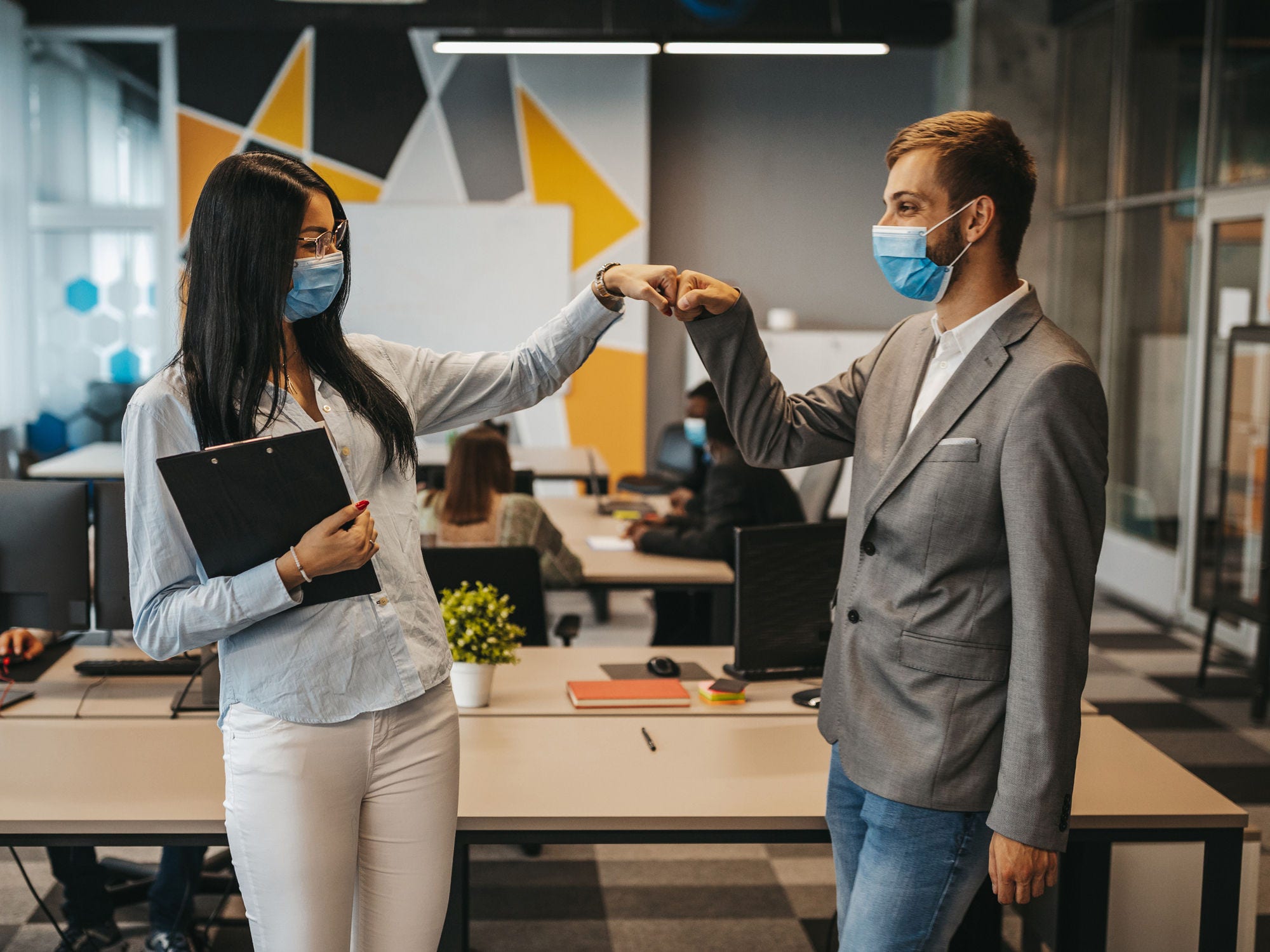 Two colleagues in masks bump fists. 