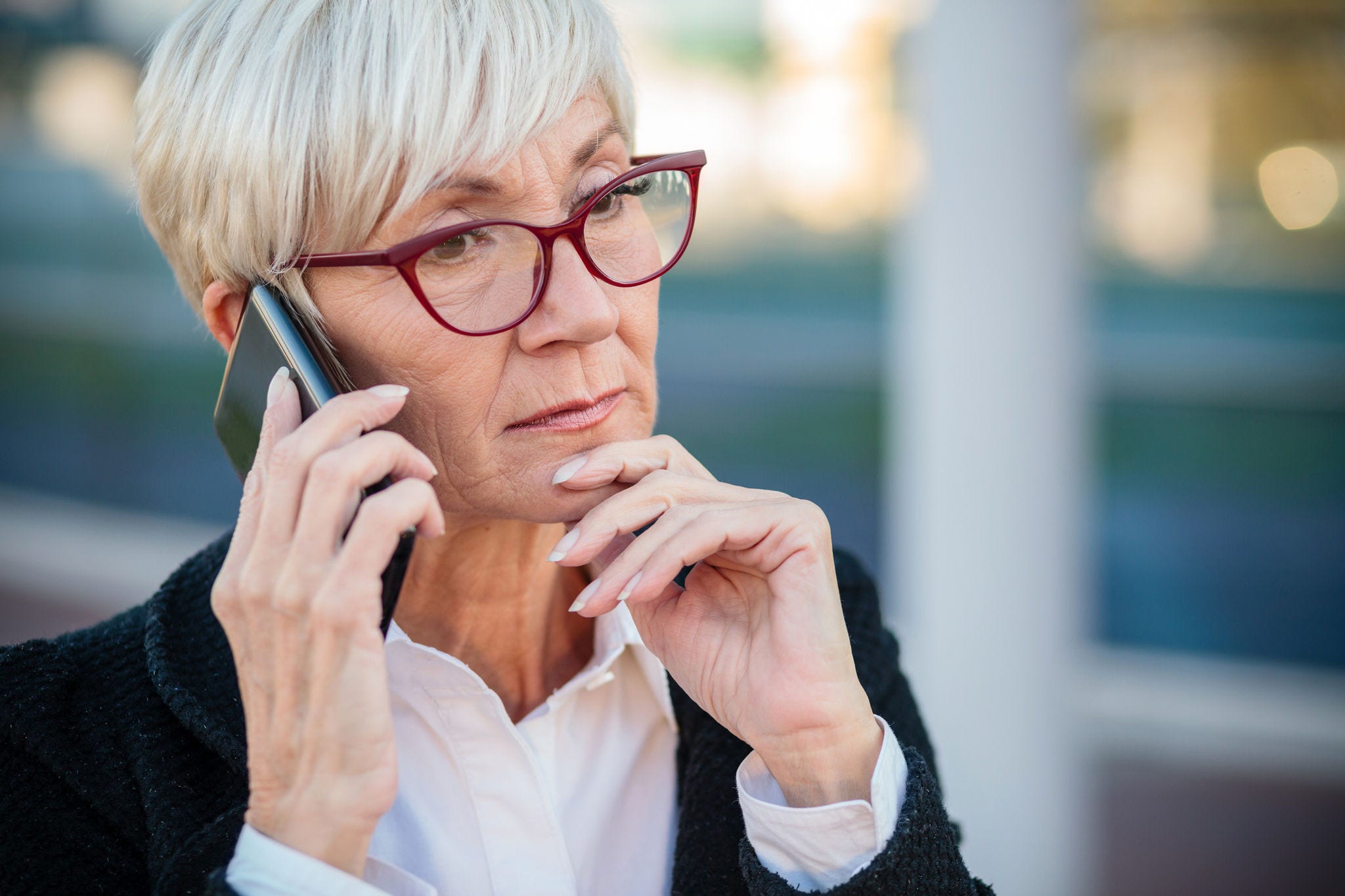 Worried mature businesswoman talking on the mobile phone, resting her arm on chin. Work anywhere concept.