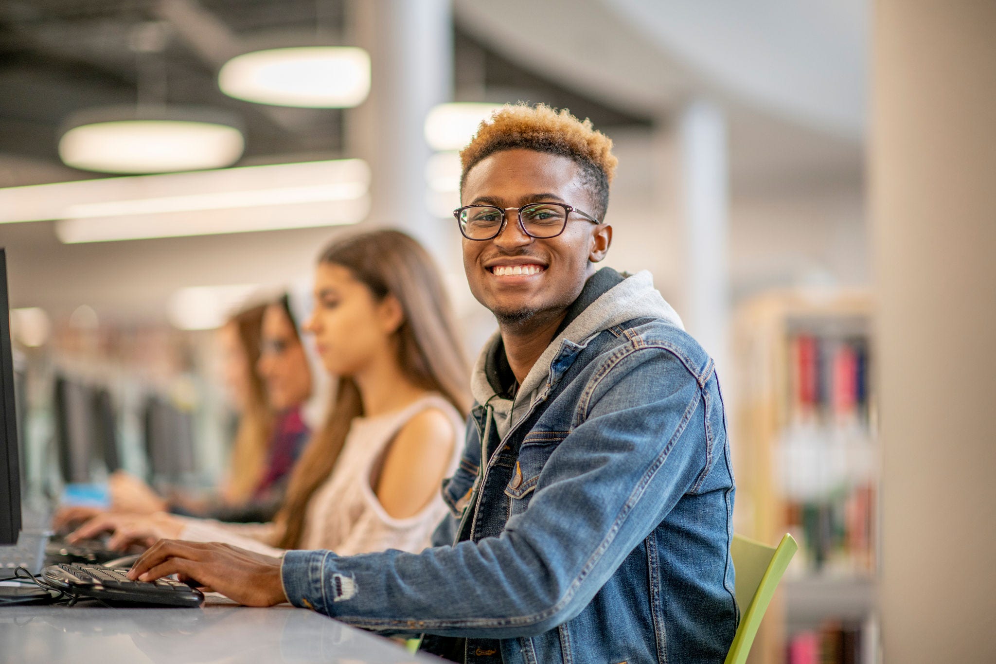 young man smiles while working at a computer next to other young people