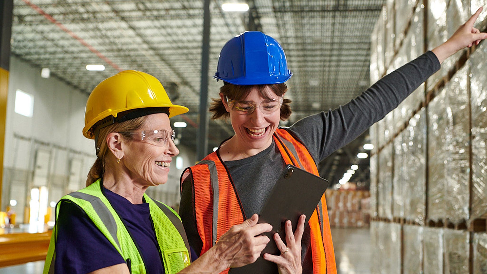 Warehouse workers smile while collaborating on a tablet.