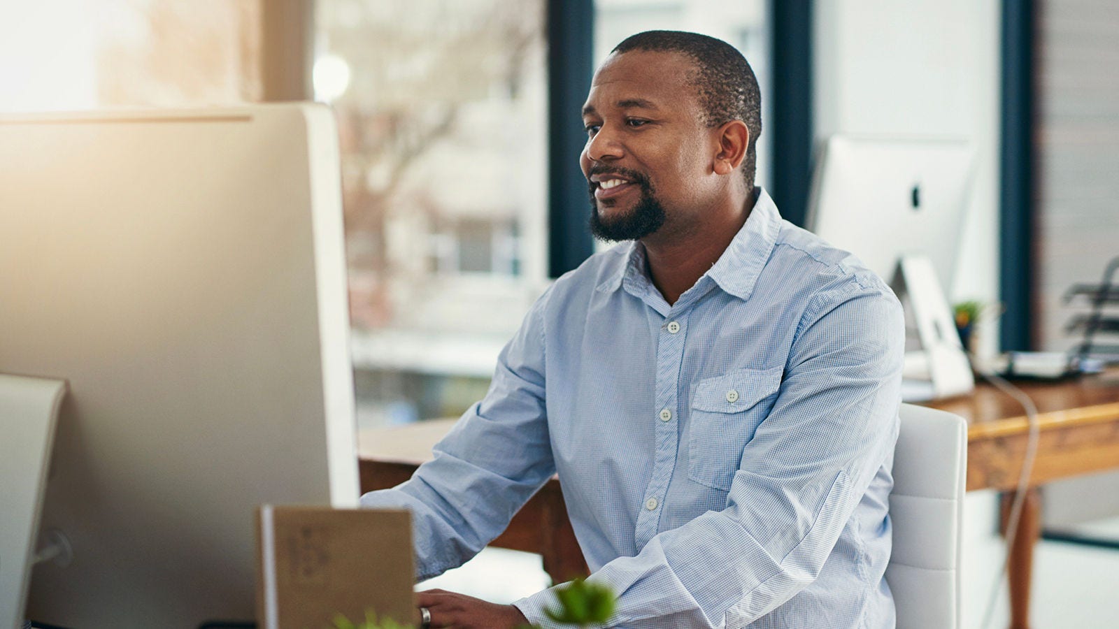 Middle-aged African American Human Resources professional working on his desktop computer within a contemporary office setting.