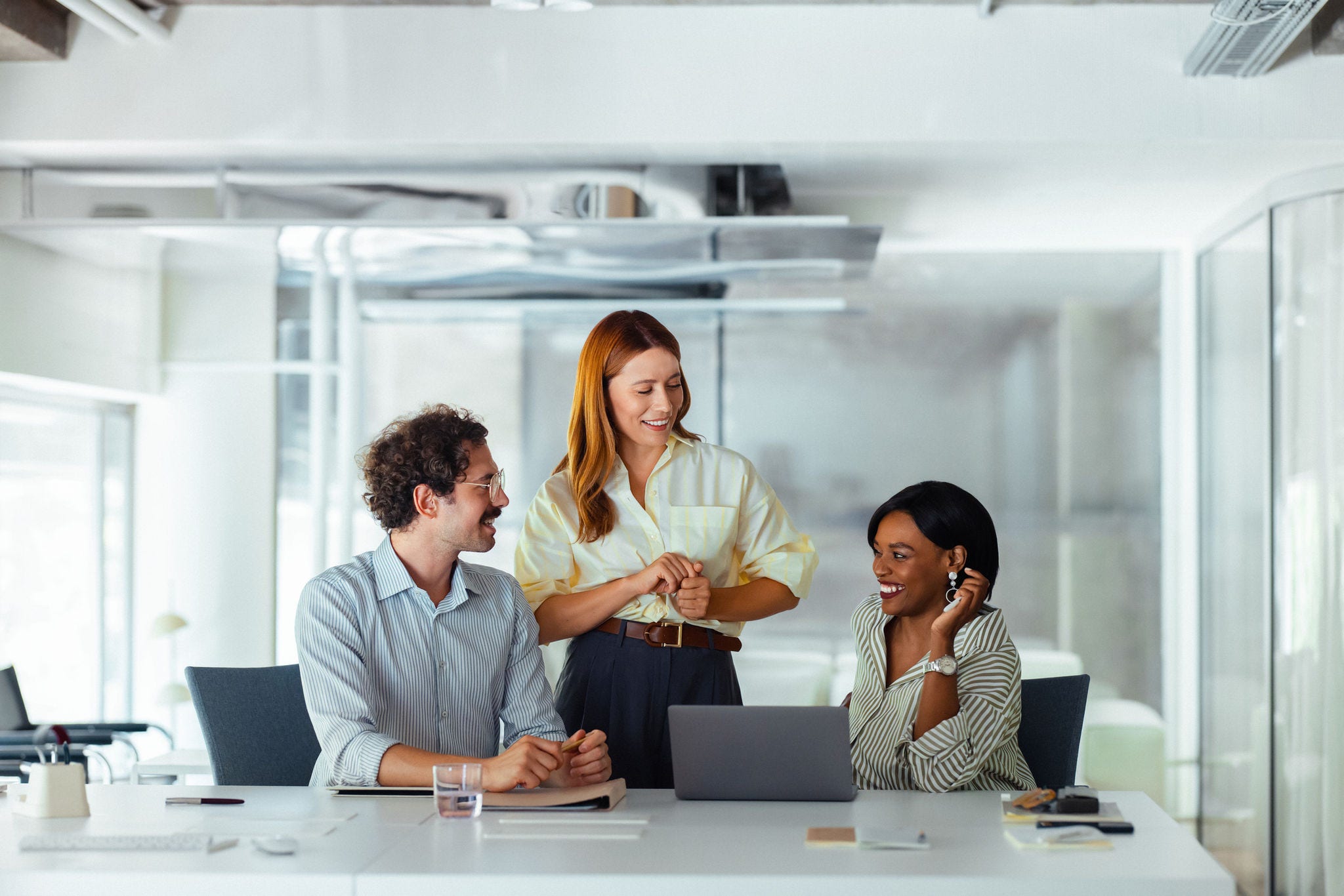 Three colleagues collaborate in a bright, modern office space, showing teamwork and communication. The atmosphere is positive and productive.