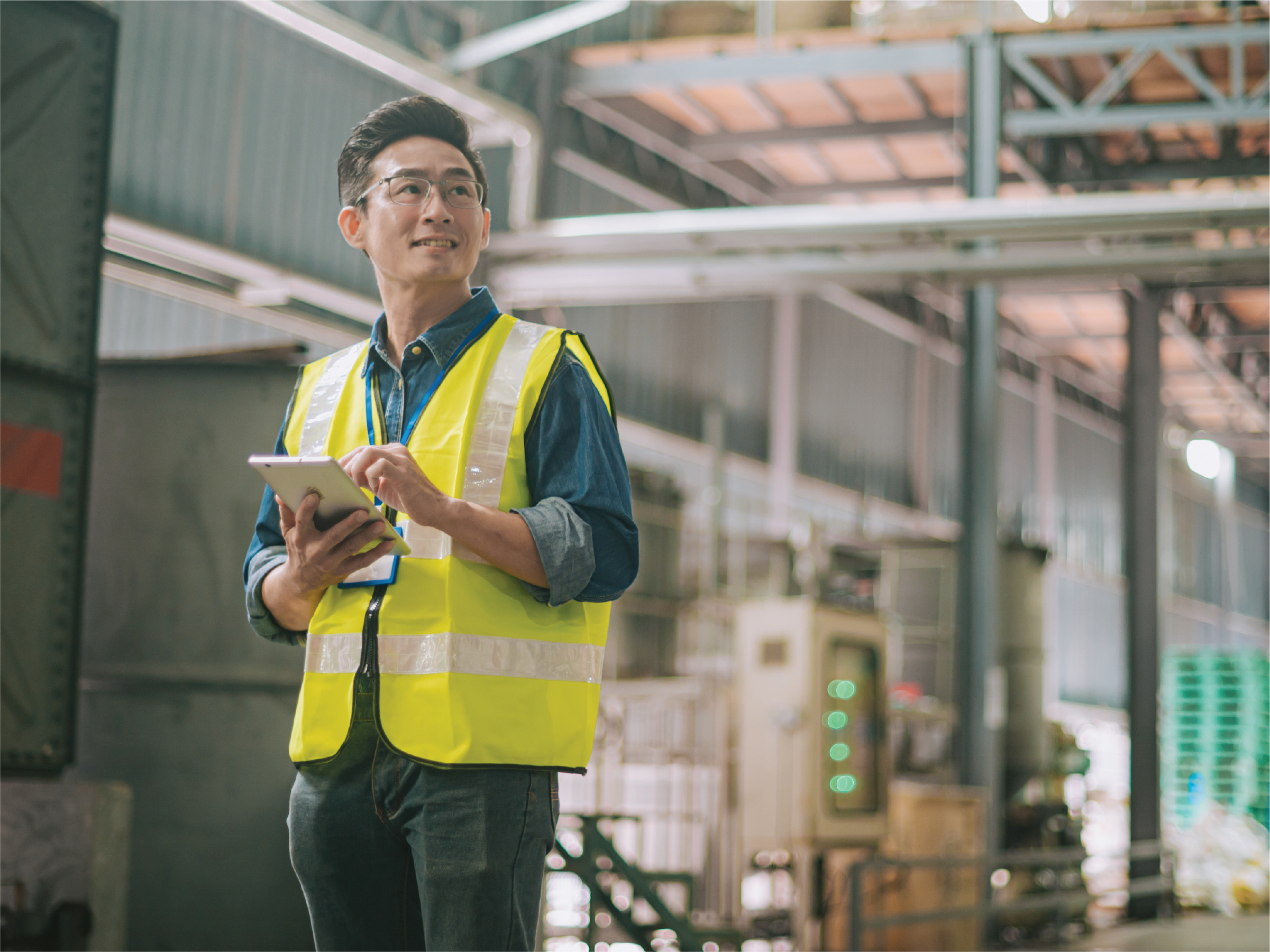man in yellow safety vest and glasses holds a tablet in a warehouse