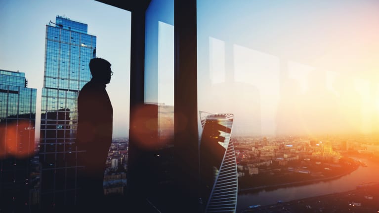 man standing in high rise looking out the window at sunset