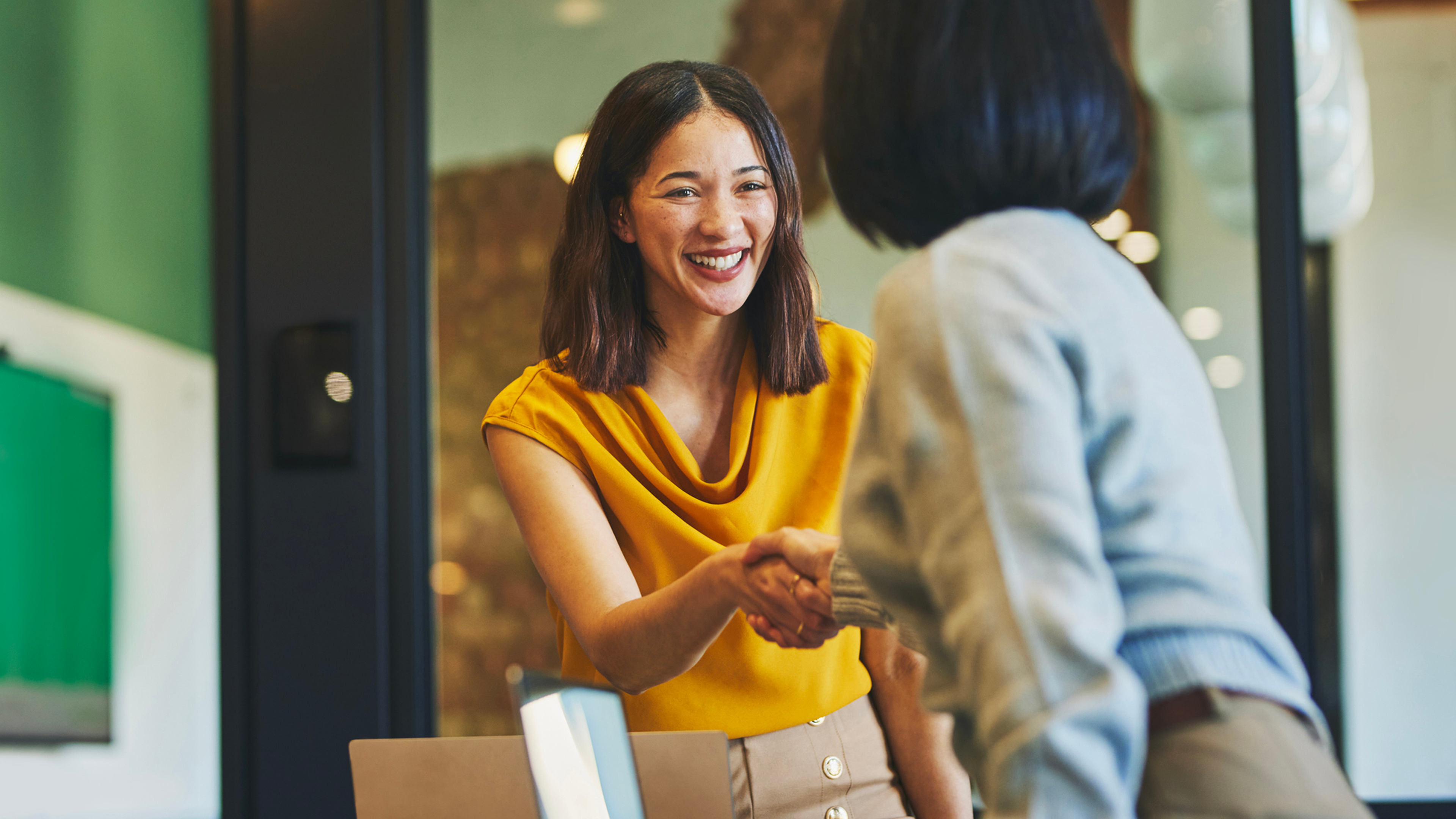 two women shaking hands at work smiling