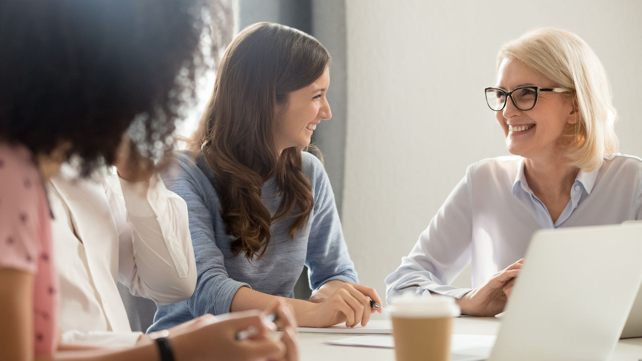Young woman and older woman smiling at each other sitting at desk