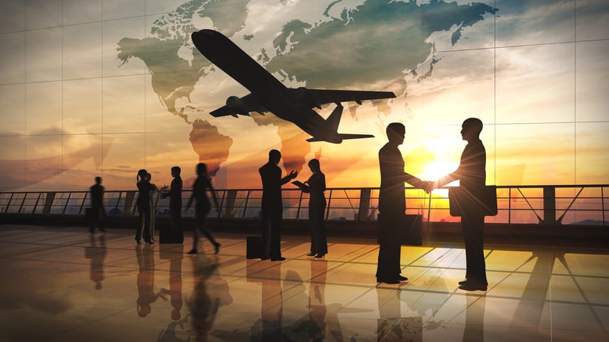 Silhouettes of business people standing in front of a plane at sunset.