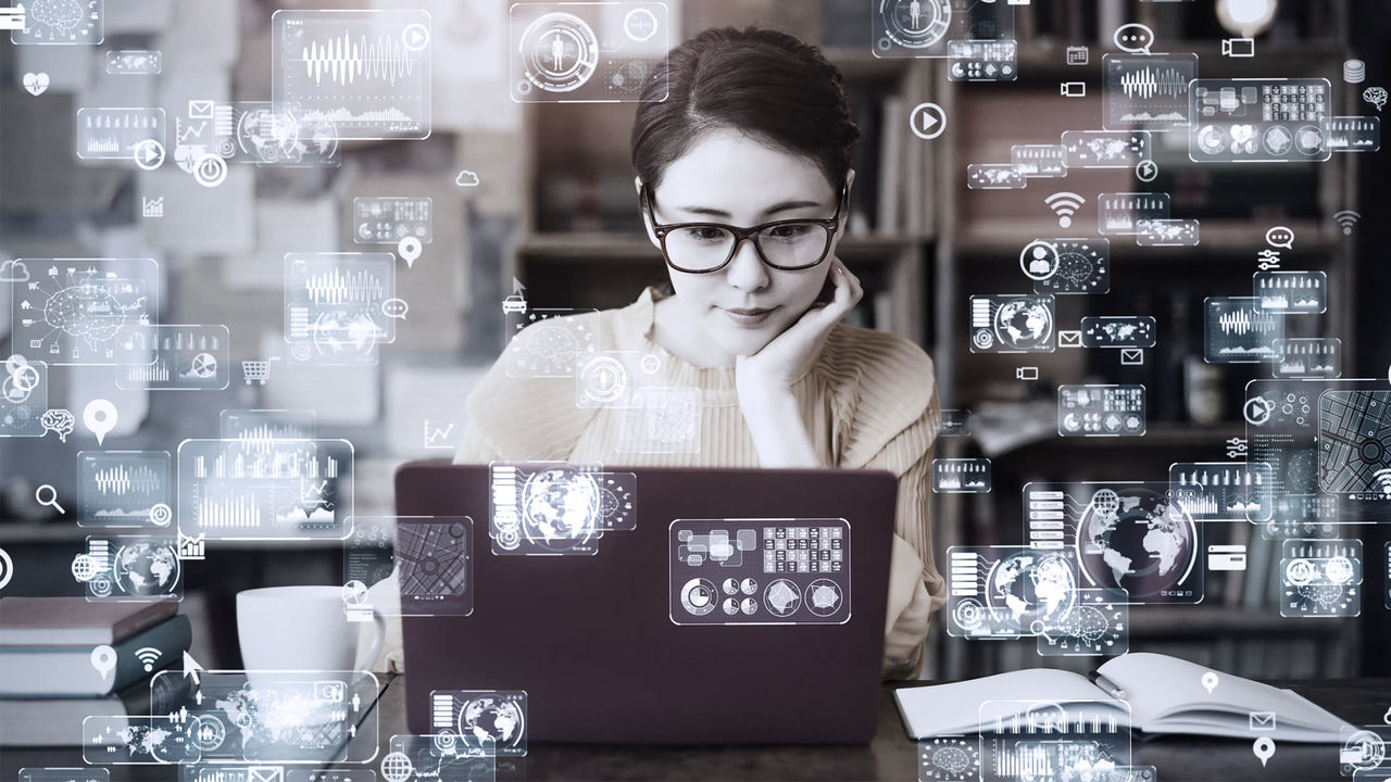 A woman is sitting at a desk with a laptop in front of her.
