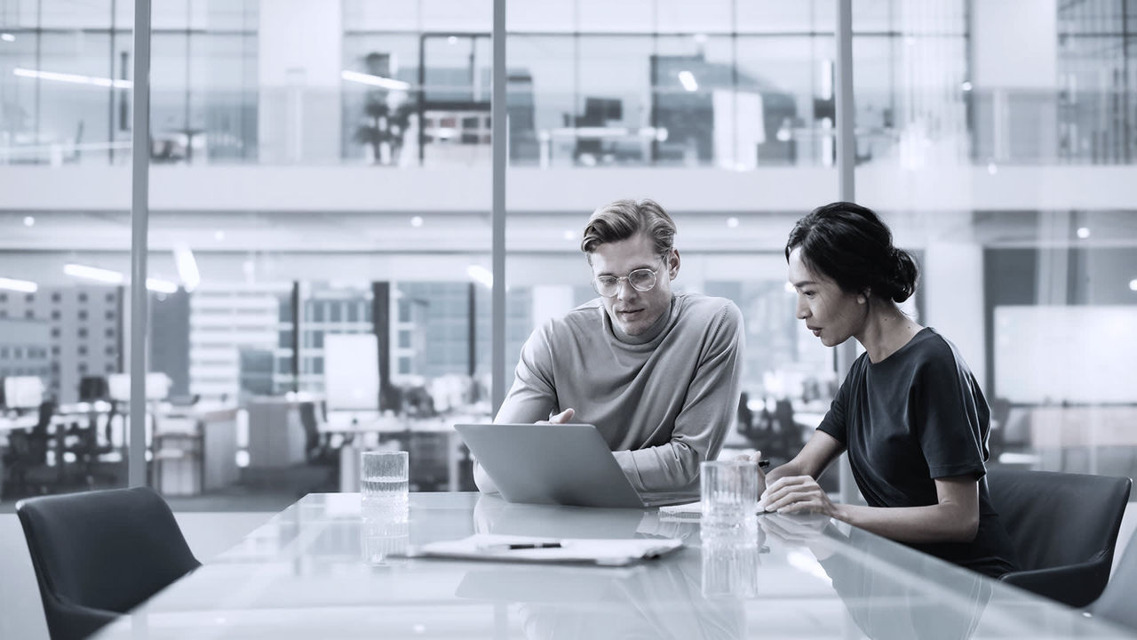 Two business people sitting at a table looking at a laptop.
