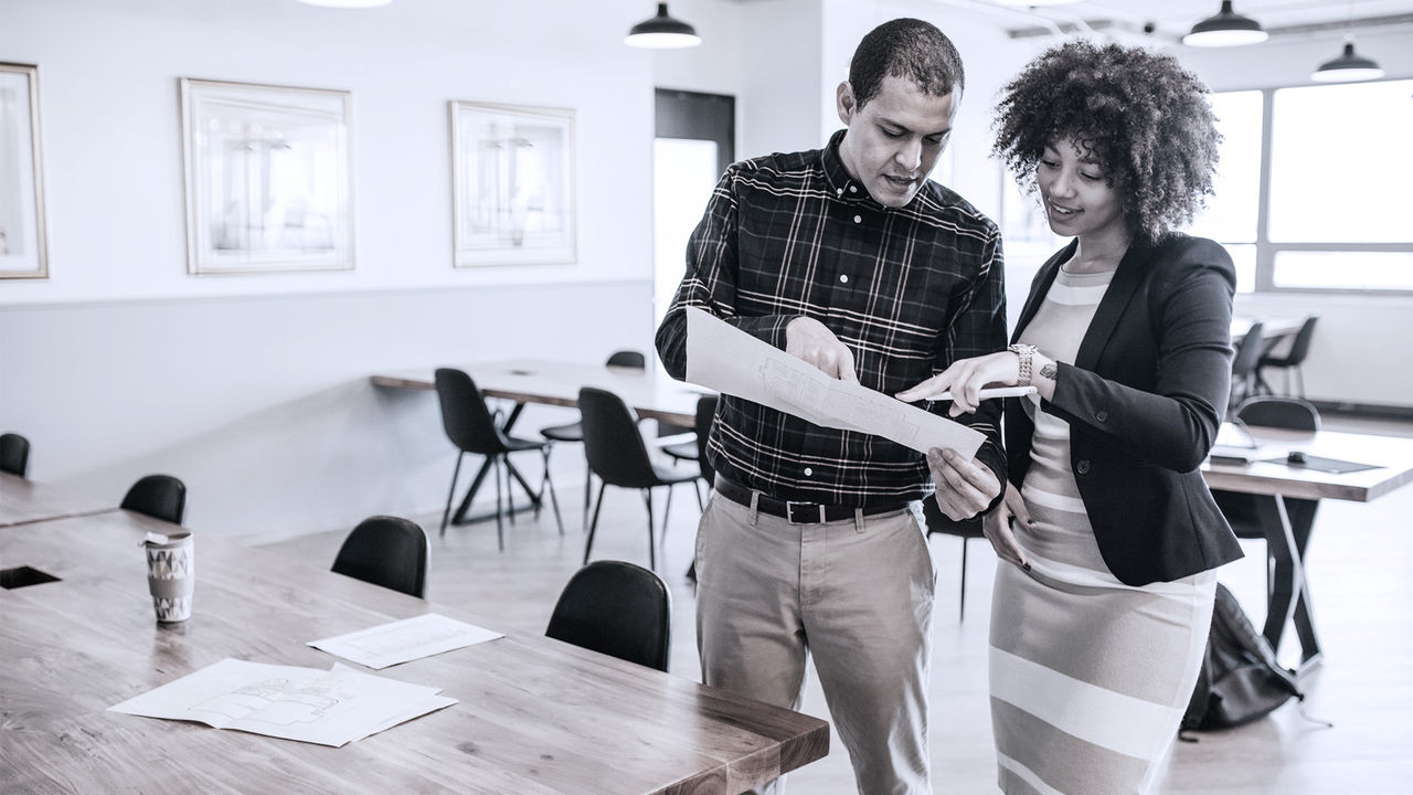 Business professional explaining a task to another employee with paper in hand