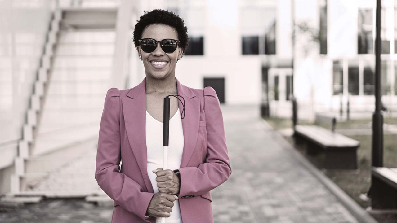 A woman wearing sunglasses and a pink blazer is holding an umbrella.