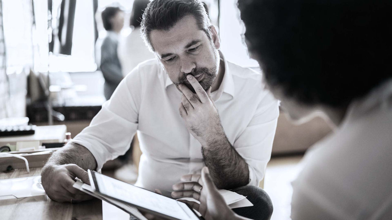 A man and woman are sitting at a table and looking at a tablet.