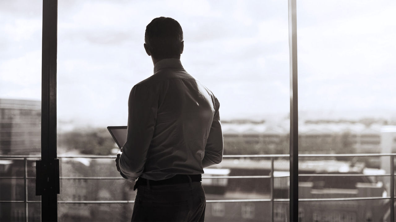 A businessman looking out of a window with a laptop.