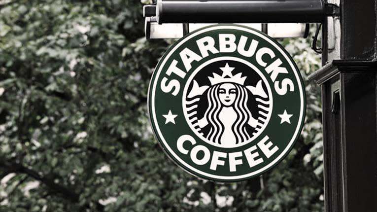 A starbucks coffee sign hangs from the side of a building.