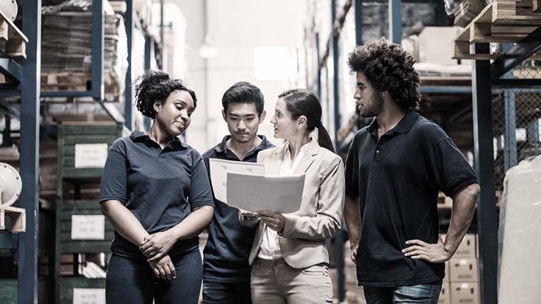 A group of people in a warehouse looking at a document.