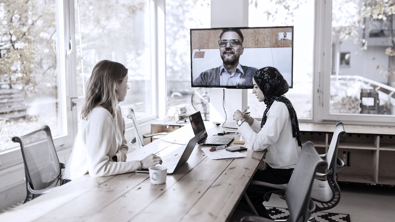 A group of people sitting at a table and talking on a video conference.