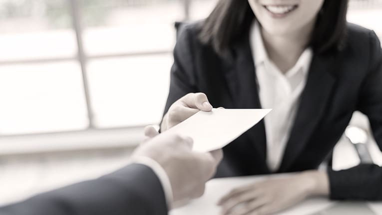 A woman handing a business card to a man in a suit.