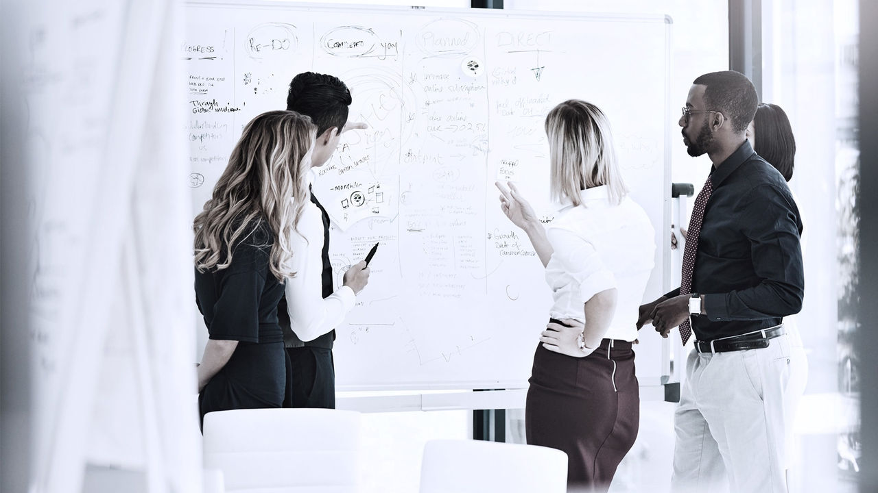 A group of business people standing around a whiteboard.